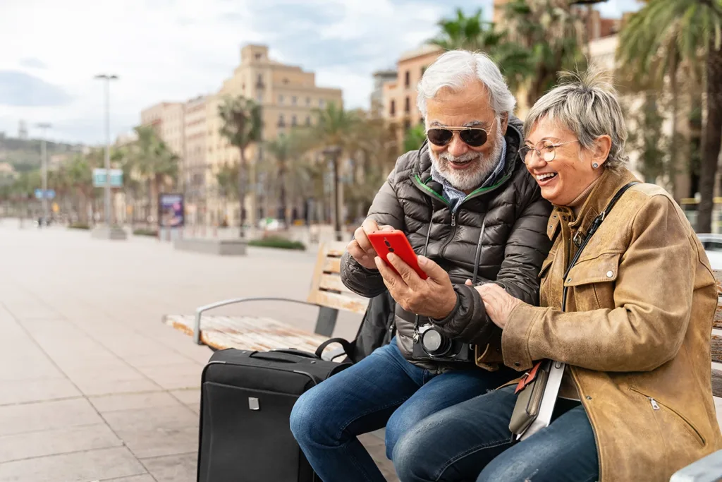 Active older adult man and woman, couple tourists traveling together using a smartphone to connect to their hearing aids with language translation capabilities
